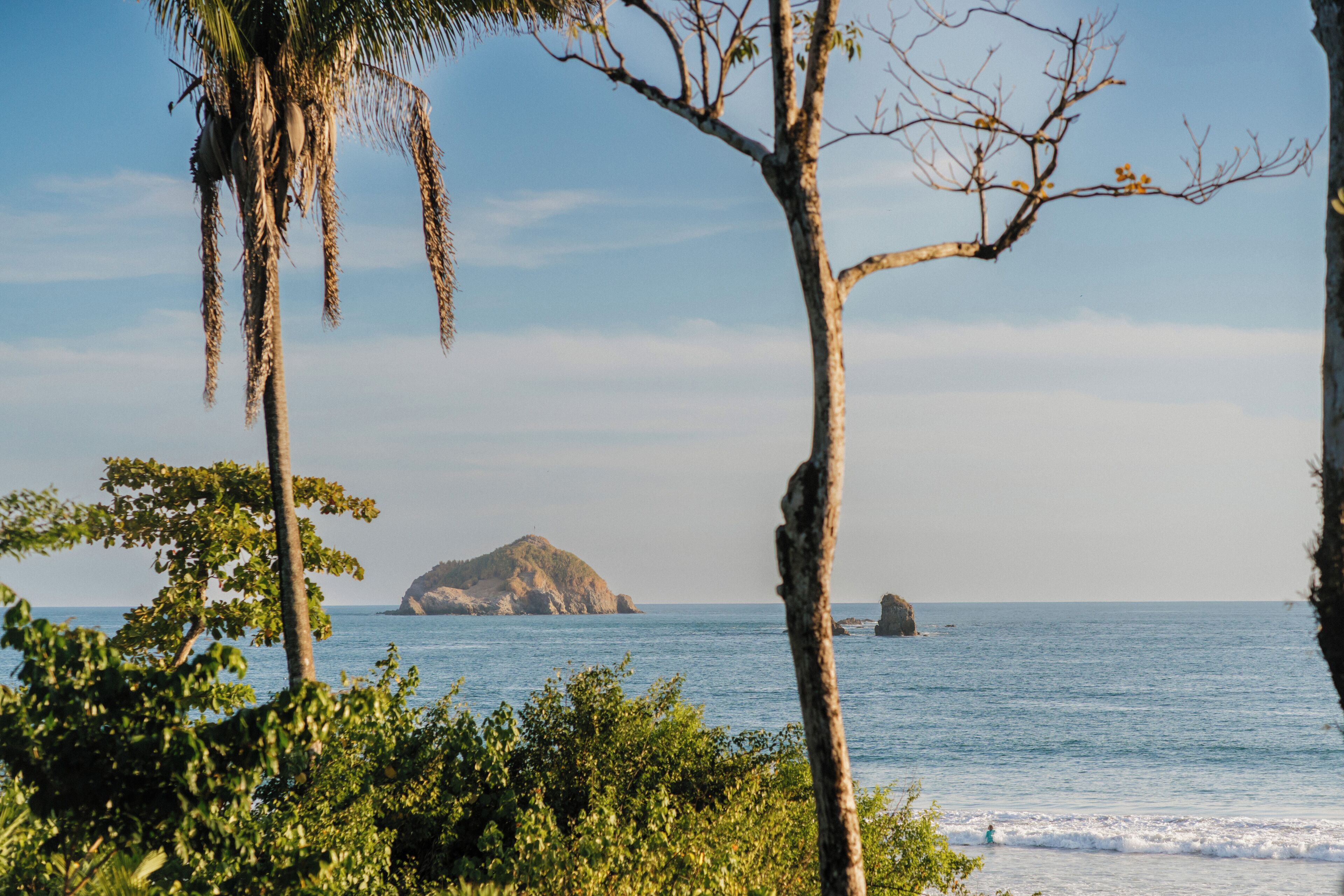 A coastal landscape with a prominent island in the distance, surrounded by lush greenery and clear blue waters.