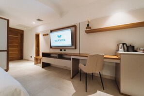 Hotelkamer met een bed, een bureau met een stoel, een televisie waarop het MIAMAR logo te zien is, een koffiezetapparaat en een plank met een vaas.