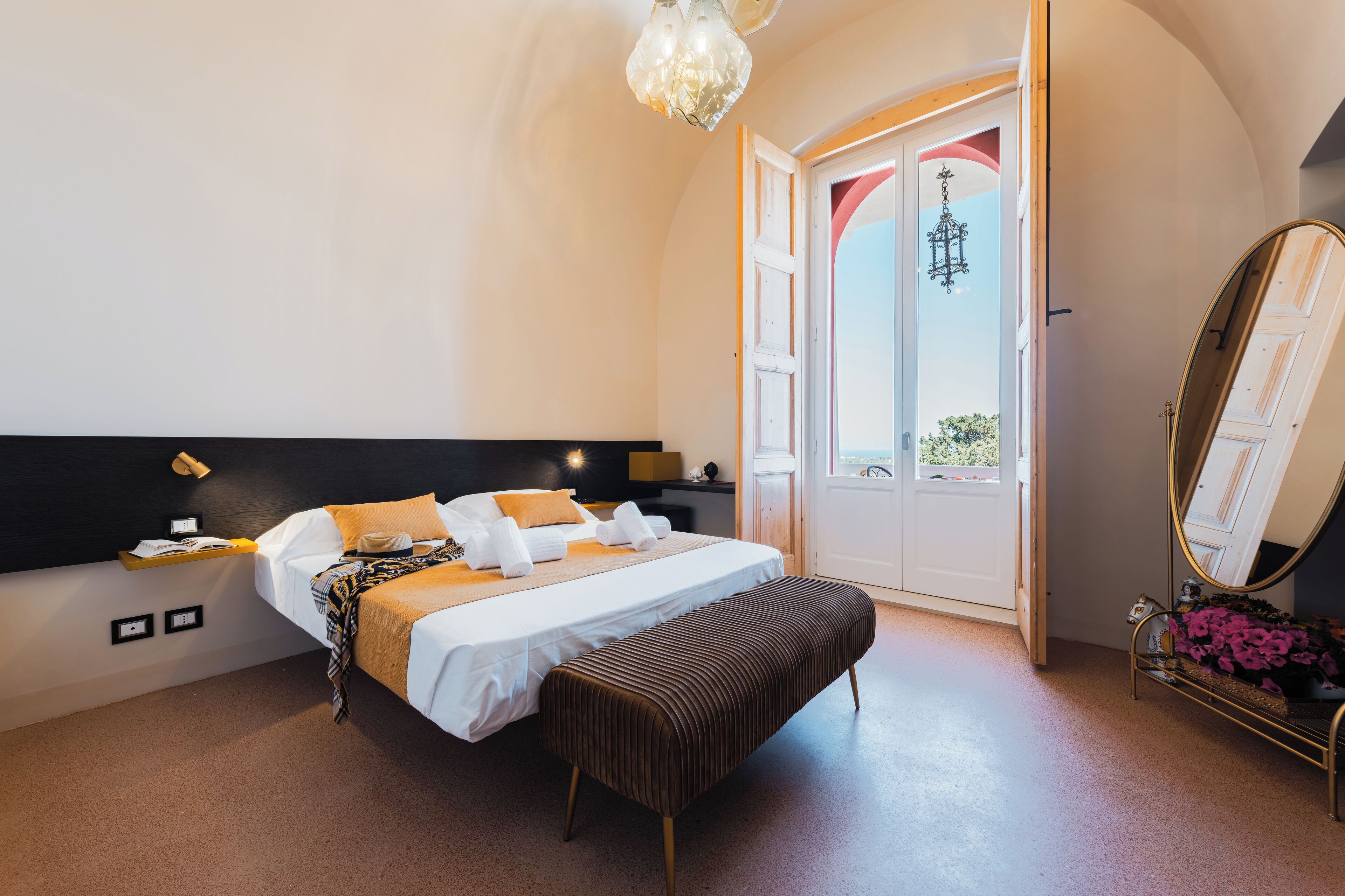 A bedroom with a bed, bedside table, bench, and a large mirror.