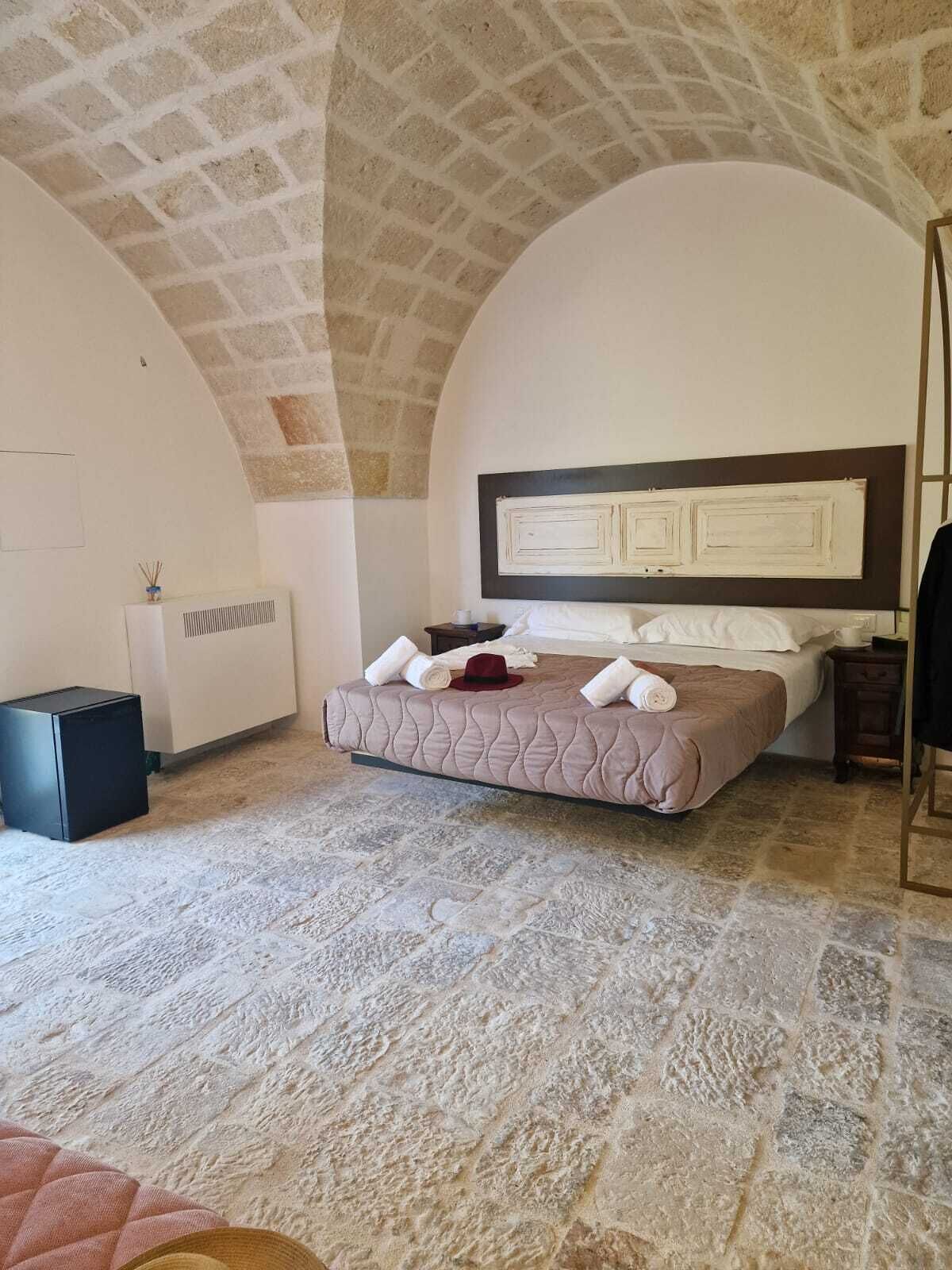 A bedroom with a stone floor, a bed with a headboard, a bedside table, and a radiator.