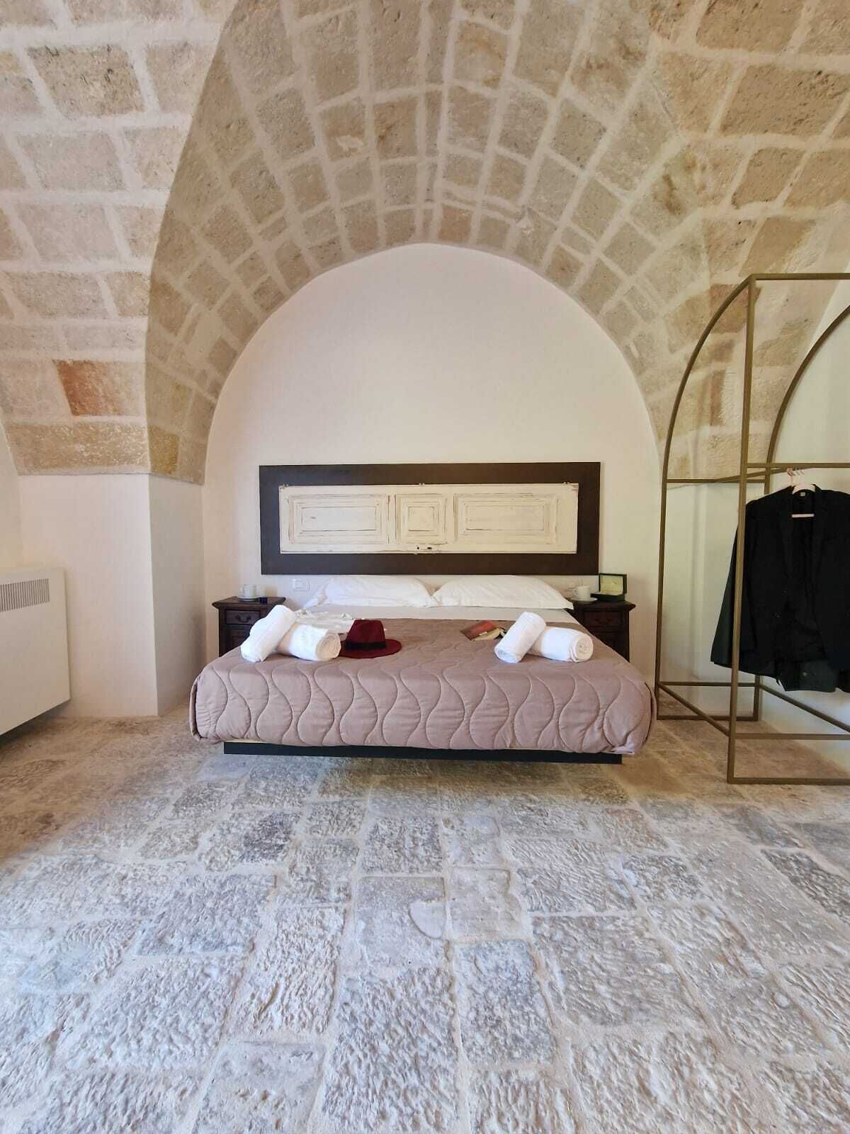 Un dormitorio con techo abovedado de piedra, cama con cabecera, mesita de noche y perchero.