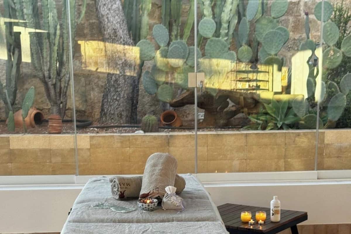 A spa area with a massage table, towels, candles, and a view of cacti through a large window.