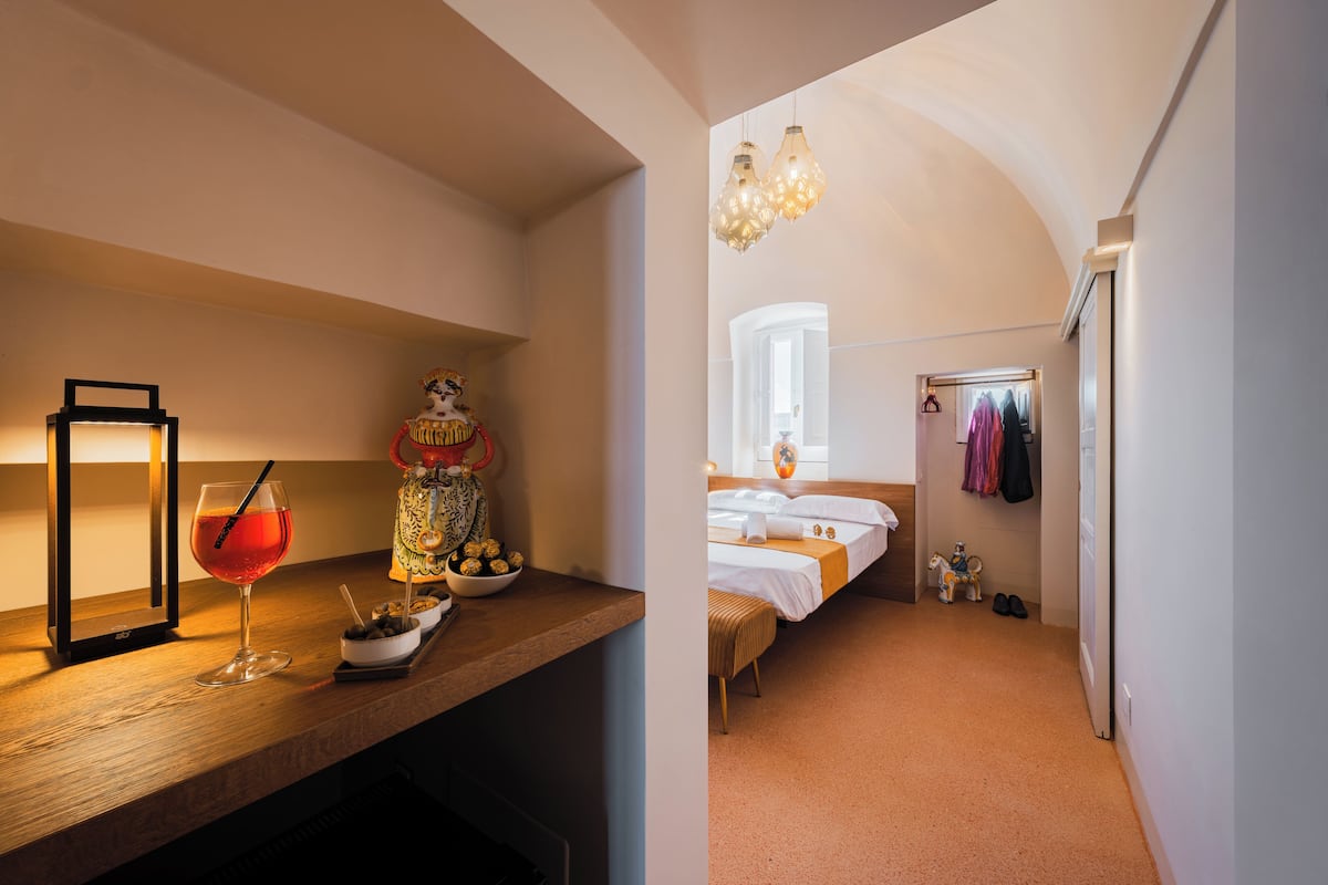 A bedroom with a bed, bedside table, lamp, and a hanging light fixture.