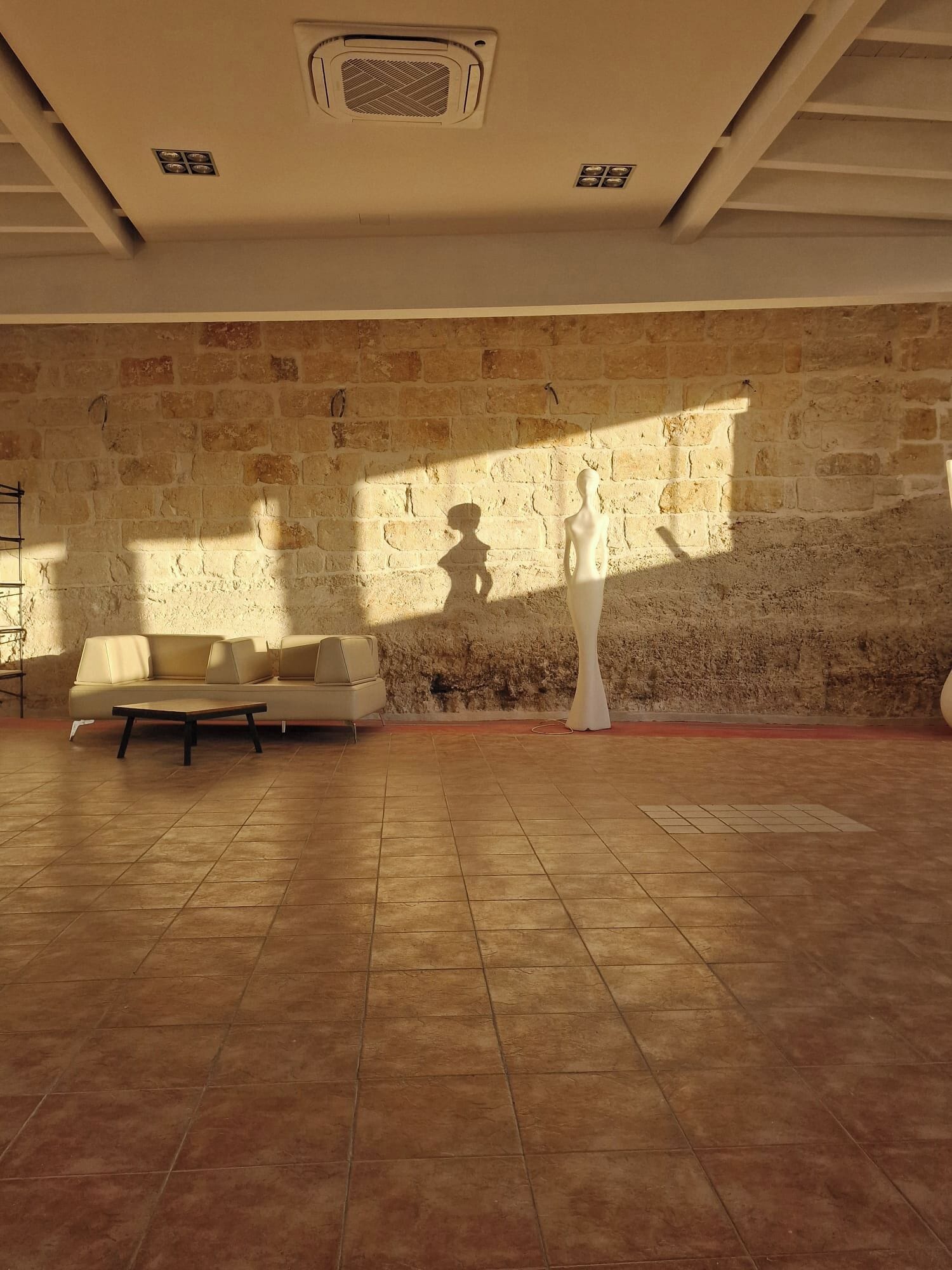 Een ruime kamer met een stenen muur, een bank en een witte sculptuur.