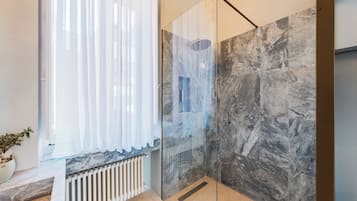 A modern bathroom with a glass shower enclosure, marble countertops, and a potted plant.