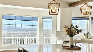 A spacious kitchen with large windows offering a city view, a central island, and two hanging pendant lights. - Luxury Retreat with Spectacular Views (Draper)