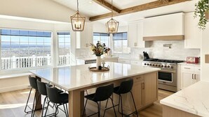 A modern kitchen with a large island, white cabinetry, and a view of the city. - Luxury Retreat with Spectacular Views (Draper)