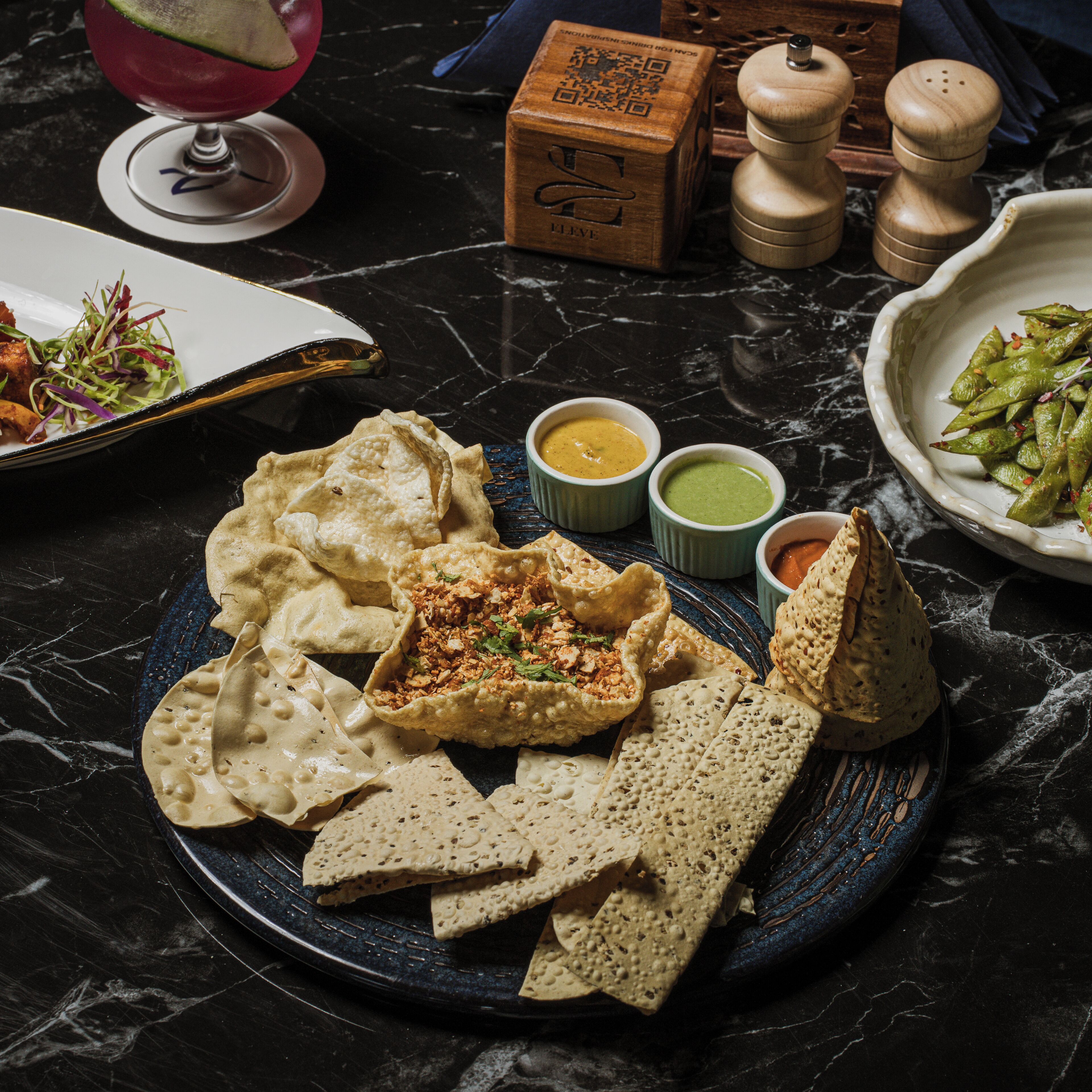 A plate of food with chips, a drink, and condiments on a marble surface.