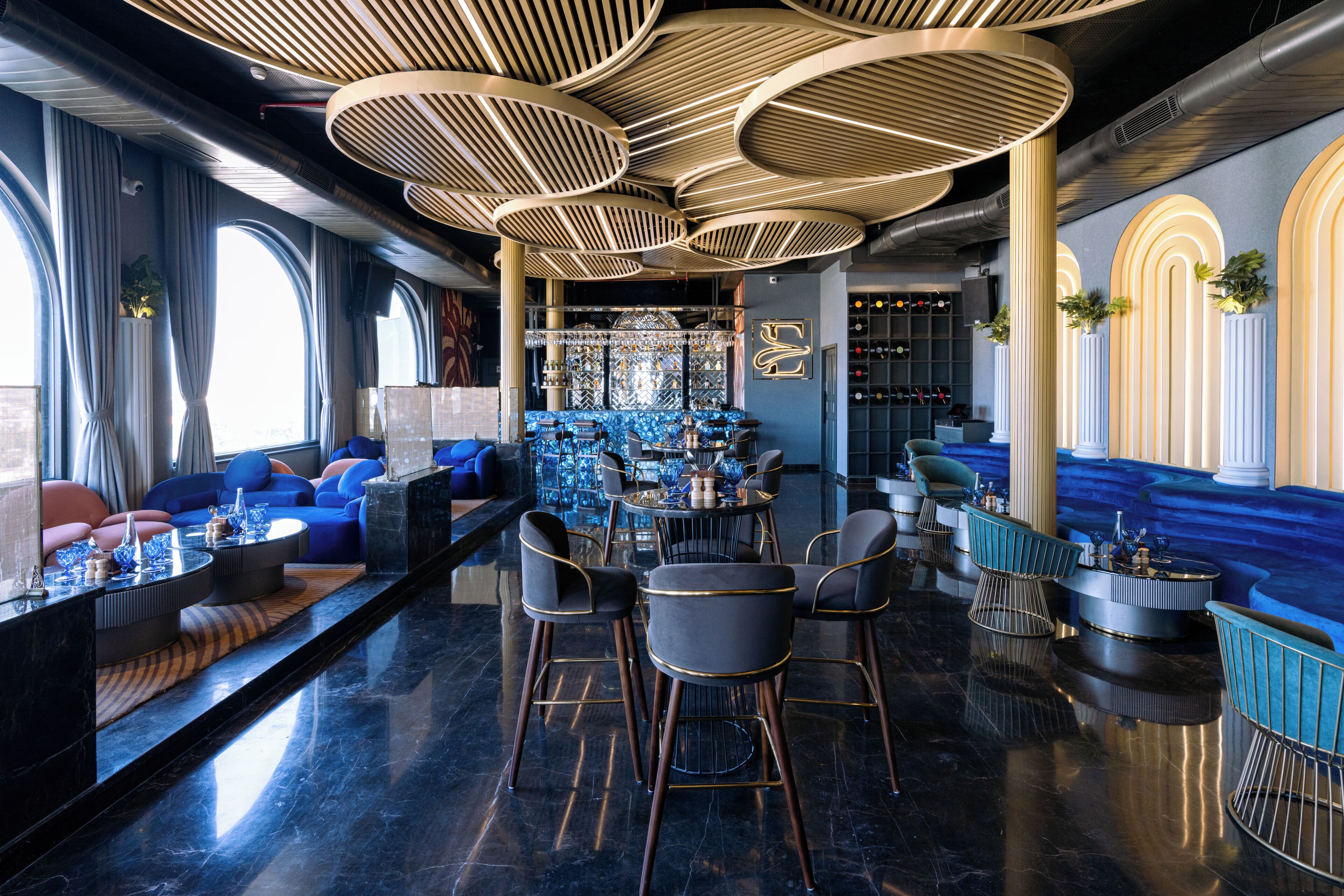 A modern bar area with high ceilings, circular light fixtures, and a bar counter with stools.