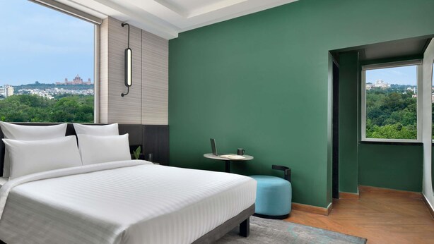 Quarto de hotel moderno com uma cama grande, uma mesa redonda pequena e vista para a cidade.