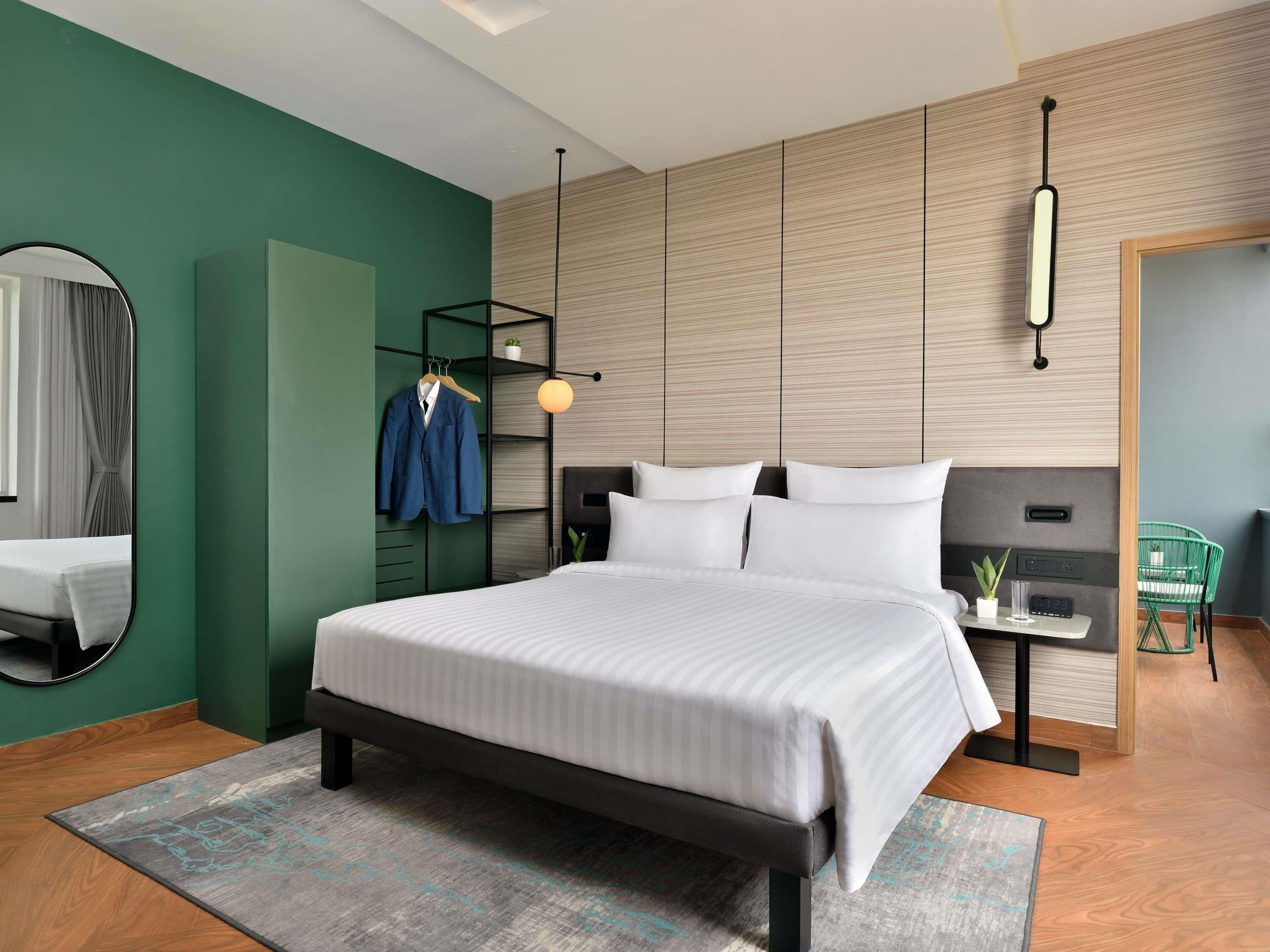Un dormitorio moderno con una cama grande, un armario, un espejo, perchero, una mesita de noche con un reloj y una silla verde.