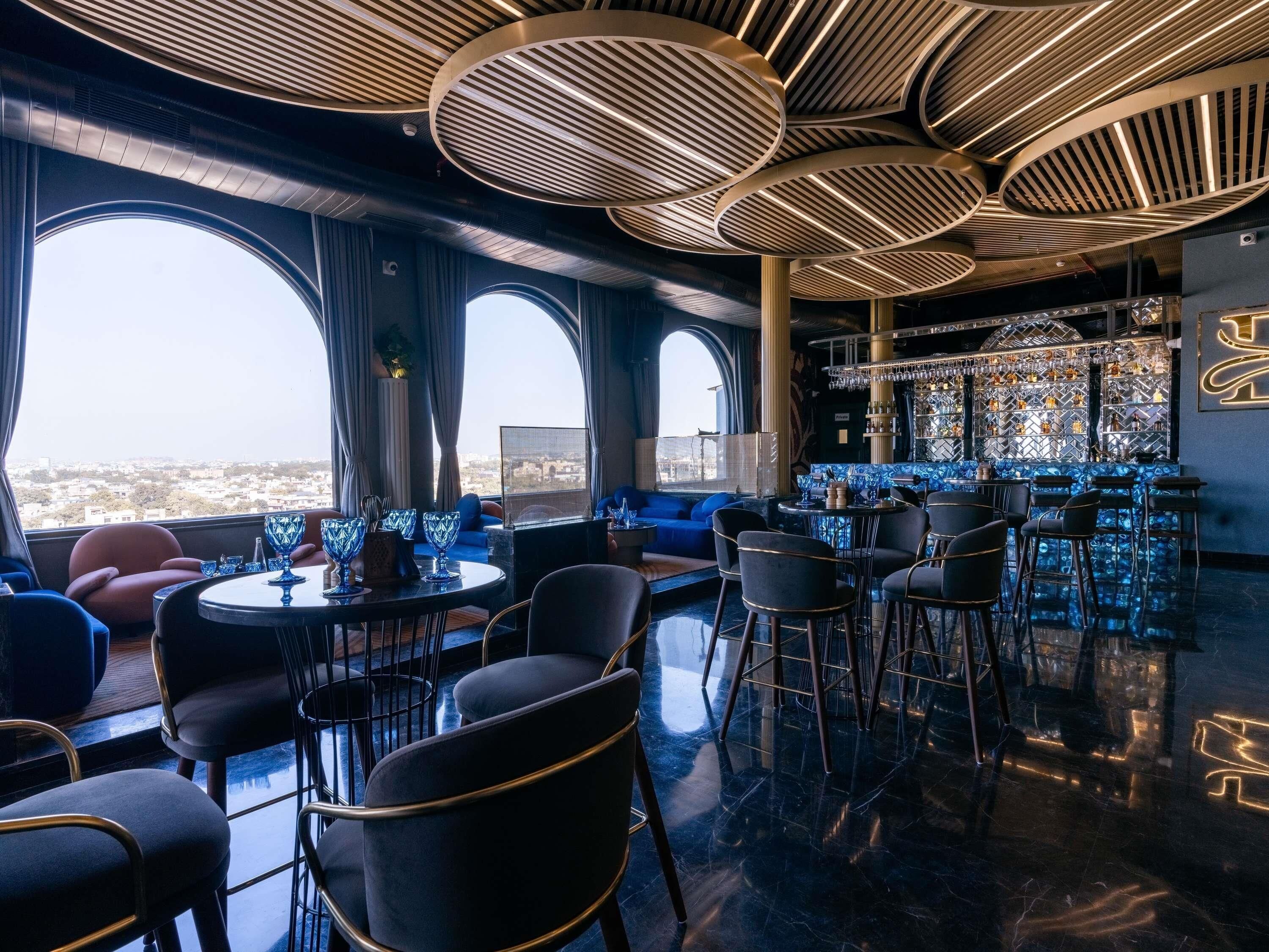Un bar moderno con vistas a la ciudad, que cuenta con una barra, zona de estar y un diseño de techo original.