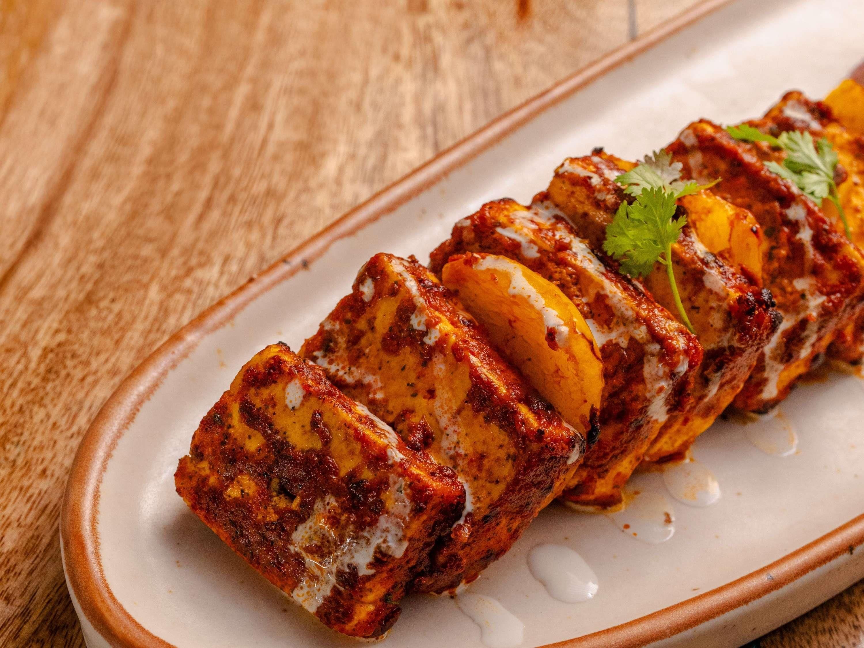 Un plat de paneer tikka nappé d’une sauce crémeuse et agrémenté d’une garniture, le tout présenté dans une assiette.