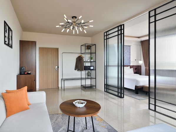 Una habitación de hotel moderna con sofá, una mesita de madera, perchero, cama y un ventanal con cortinas.