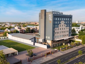 A modern hotel with a prominent 'NOVOTEL' sign, a spacious parking area, and a well-maintained lawn.