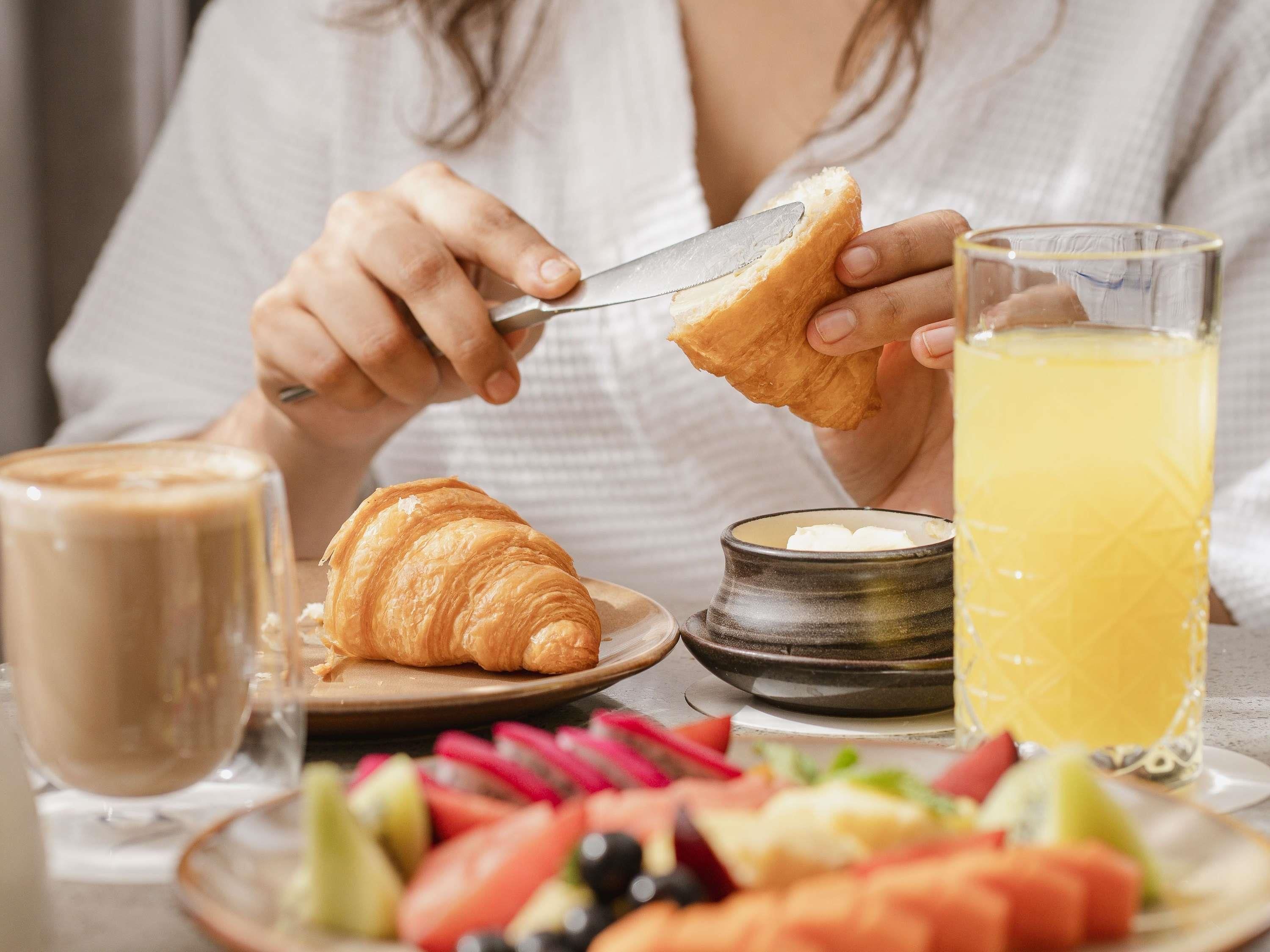 A person cutting a croissant, a glass of orange juice, and a plate of fruit.