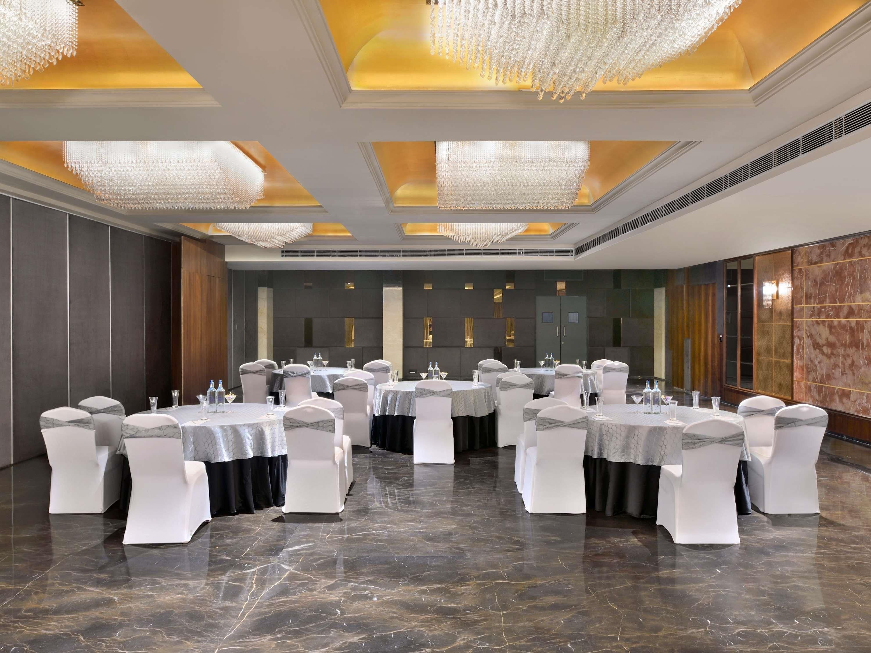 Uma sala de banquetes com mesas redondas, cadeiras brancas e lustres.