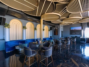 A modern bar area with high ceilings, circular light fixtures, and a seating arrangement with bar stools and tables.