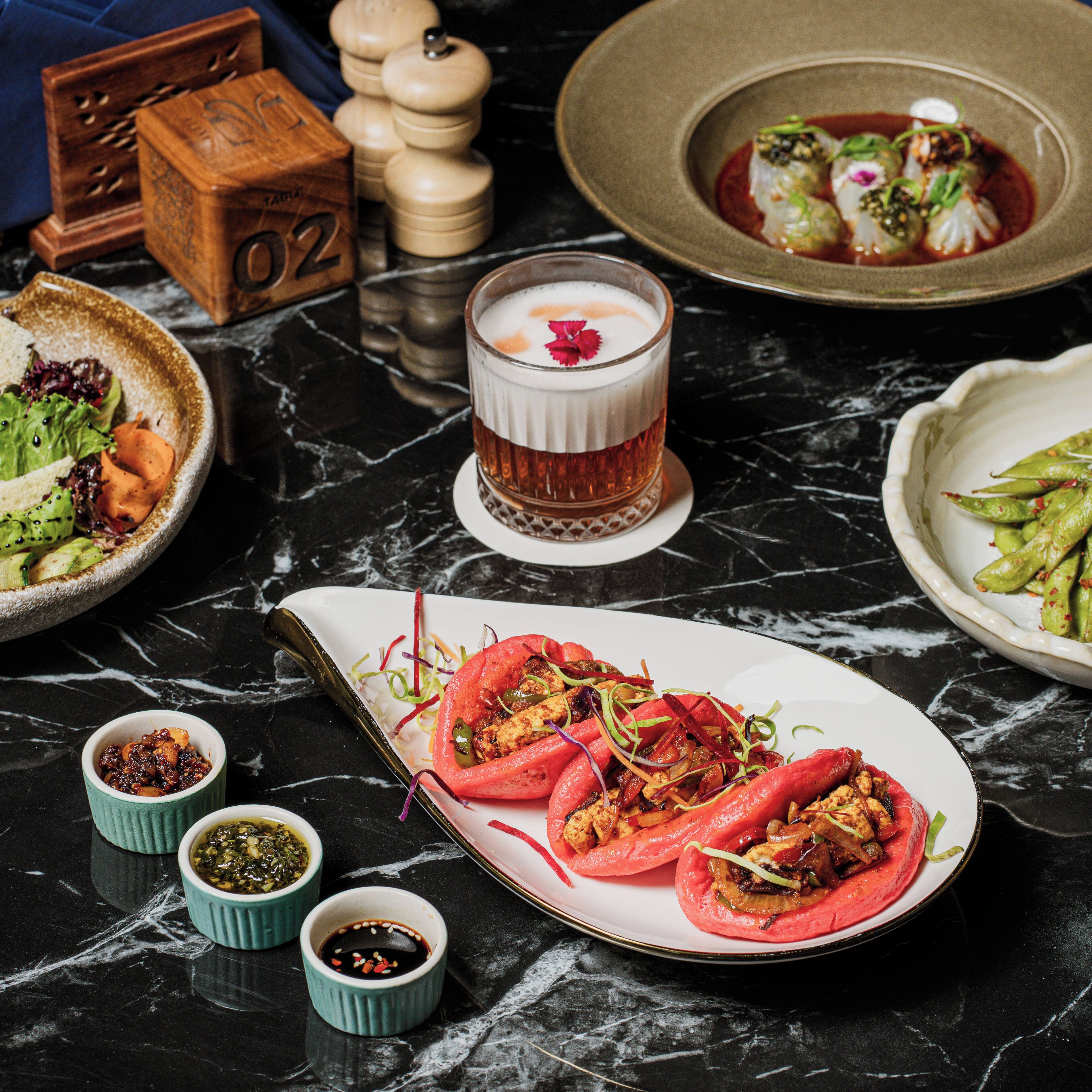 A dining table with various dishes, including tacos, a glass of a beverage, and condiments.