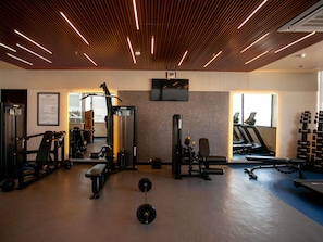 A gym with exercise equipment, a bench, a treadmill, and a wall-mounted TV. - Novotel Jodhpur Iti Circle (Jodhpur)