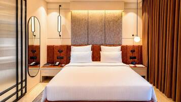 A modern hotel room with a large bed, bedside tables, a mirror, and a wall-mounted light fixture.