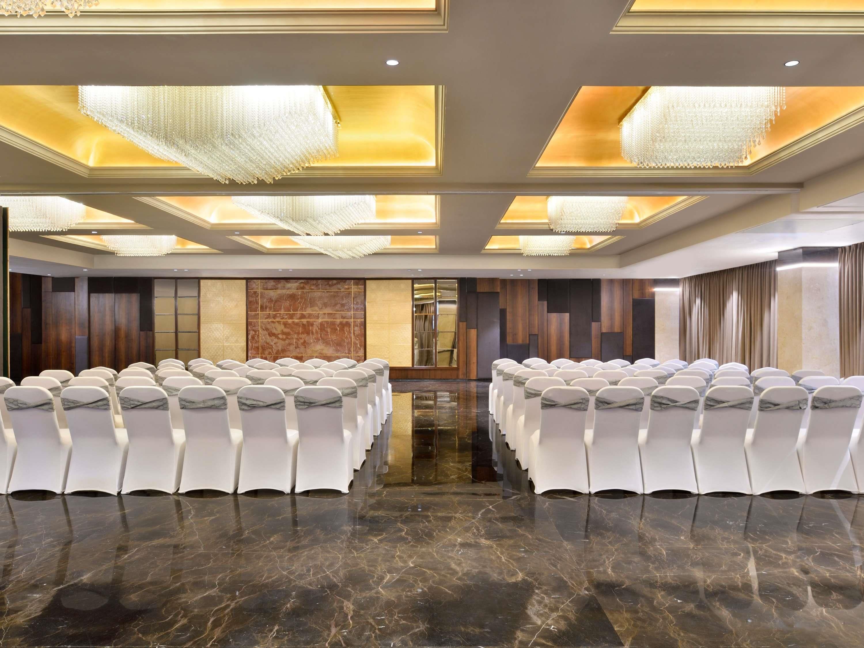 A conference room with rows of white chairs, a marble floor, and a chandelier.
