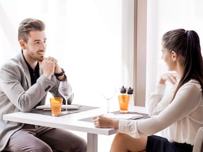 A man and a woman sitting at a table with drinks, a laptop, and a bottle of orange juice. - Novotel Jodhpur Iti Circle (Jodhpur)