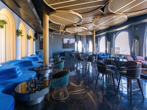 A modern lounge with blue seating, a TV, and a city view. - Novotel Jodhpur Iti Circle (Jodhpur)