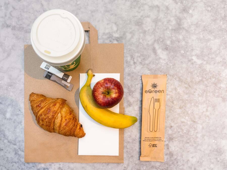 Ein Croissant, ein Apfel, eine Banane, eine Kaffeetasse und ein Serviette auf einer Marmorplatte.
