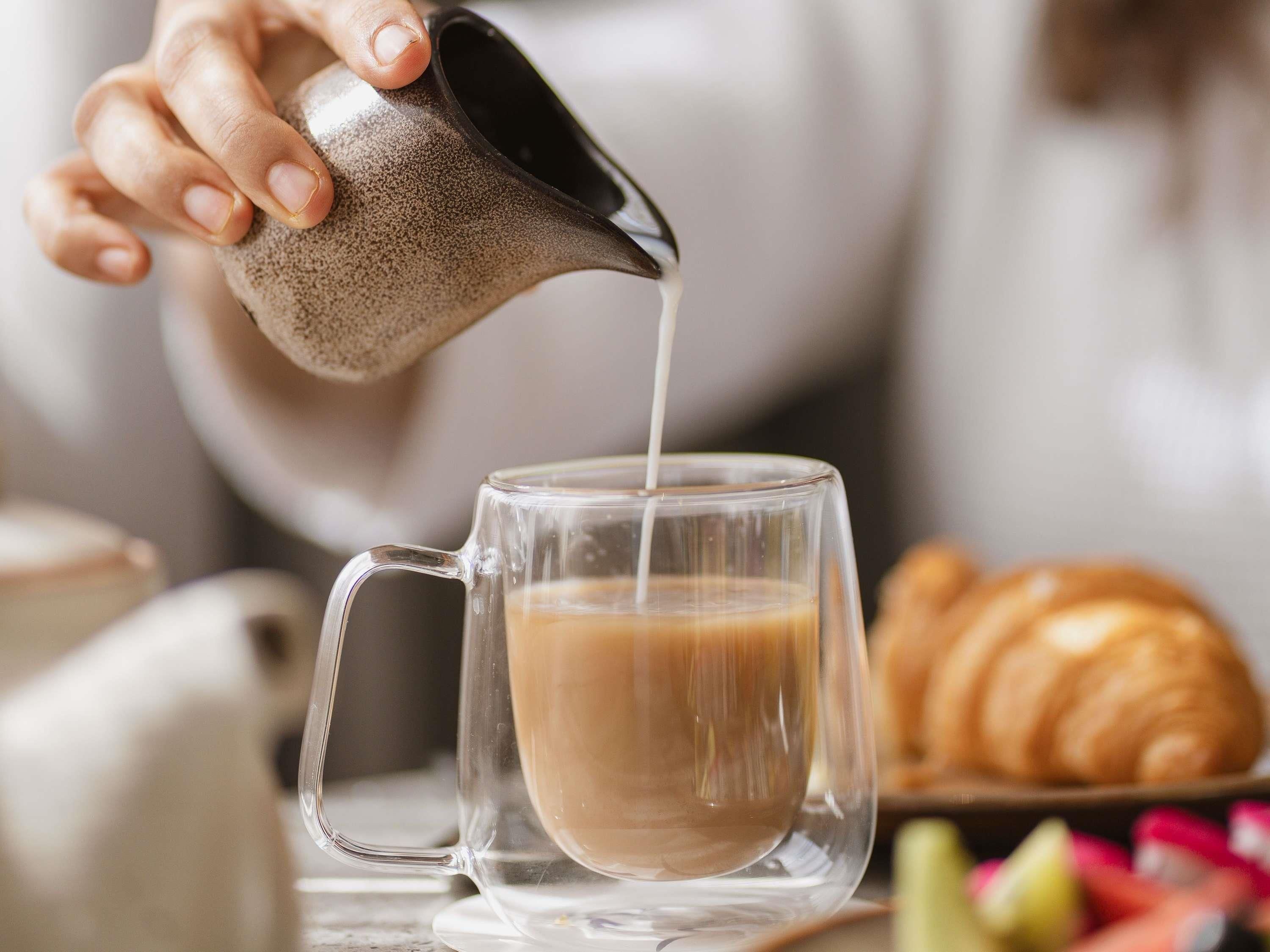 A hand pouring a liquid into a clear glass mug.