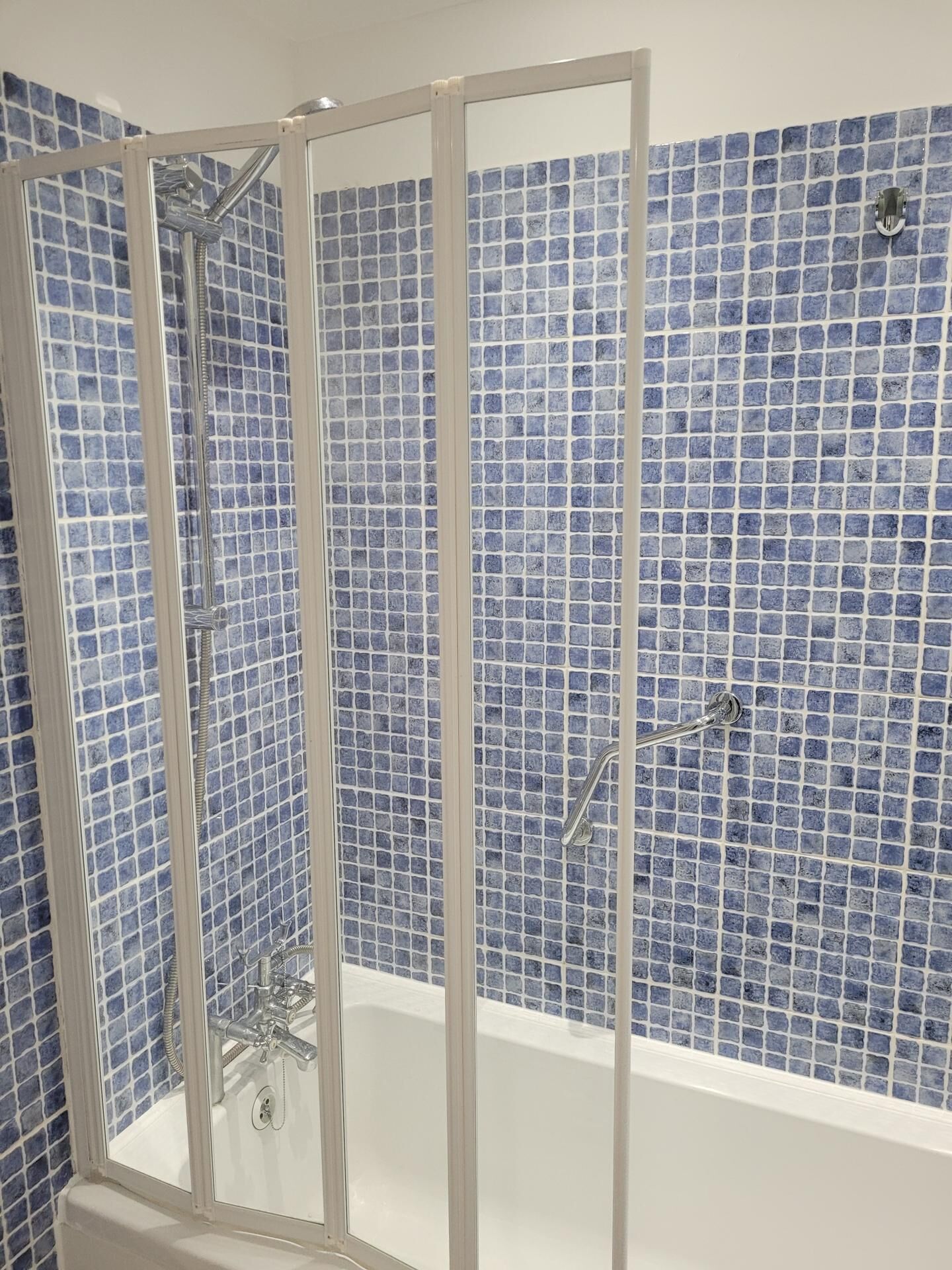 A bathroom with a glass-enclosed shower, a white bathtub, and blue mosaic tiles on the walls.