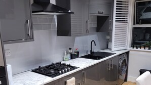 A modern kitchen with grey cabinets, a black stove, a sink, and a window with blinds.