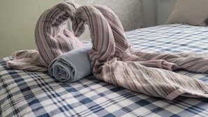 A bed with a checkered bedspread and a rolled towel.