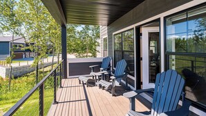 Eine überdachte Terrasse im Freien mit Adirondack-Stühlen, Holzboden und Blick auf eine Wohngegend mit Bäumen und Häusern.