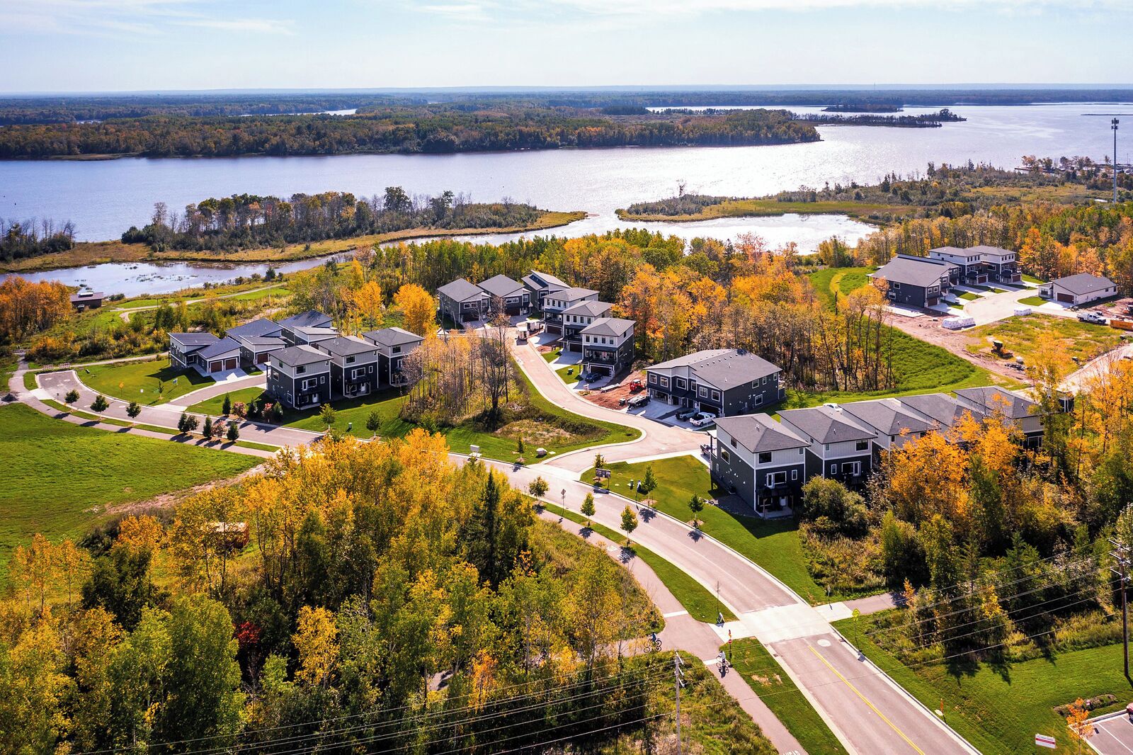 A residential area with modern houses, a road, and a body of water in the background.