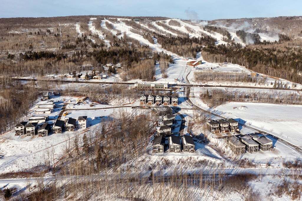 Un paisaje nevado con un conjunto de edificios, probablemente un complejo turístico o una cabaña, y una pista de esquí al fondo.