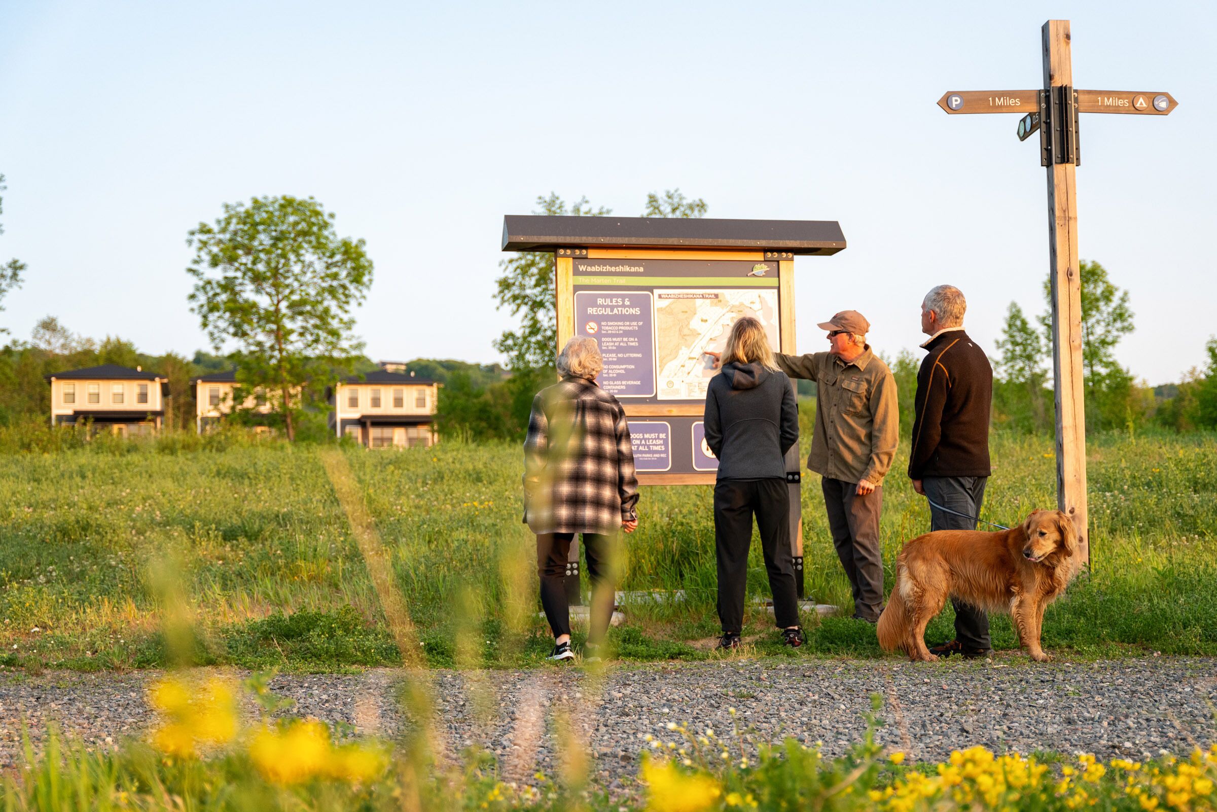 A group of people standing near a signpost with a map and information board in a grassy field.