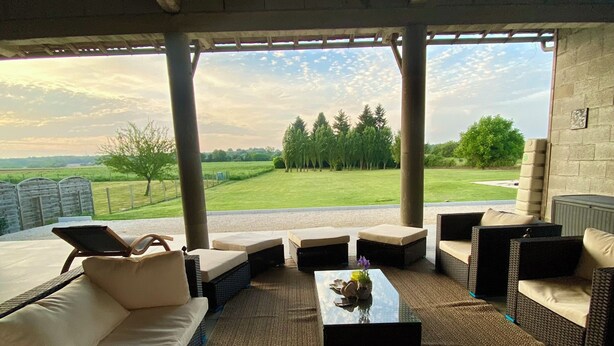 Un espace extérieur aménagé avec des canapés et des fauteuils, une table basse et une vue sur un champ verdoyant et des arbres.
