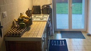 Une cuisine avec un plan de travail recouvert de carreaux, une cuisinière, une machine à café et un panier de fruits.
