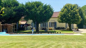 Une pelouse bien entretenue, un espace extérieur aménagé avec des sièges et un bâtiment doté d’un toit en tuiles.
