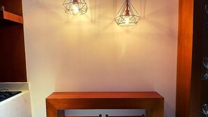 A kitchen area with a wooden counter and two stools, two hanging pendant lights, and a white wall. - Calle 76 Estudio by Caribecheap (Barranquilla)