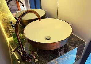 Un baño con un lavabo de cobre redondo sobre una encimera de mármol, un grifo y un espejo.