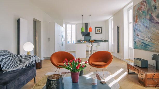 A modern living room with a sofa, two orange chairs, a coffee table with a vase of red flowers, and a kitchen in the background. - Bright, quiet apartment in the heart of Biarritz (Biarritz)
