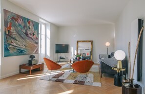 A modern living room with a large abstract painting, a flat-screen TV, a round table with a lamp, and a sofa.