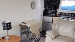 Ett kompakt bostadsutrymme med ett litet kök, ett matbord med stolar, en soffa och en lampa.