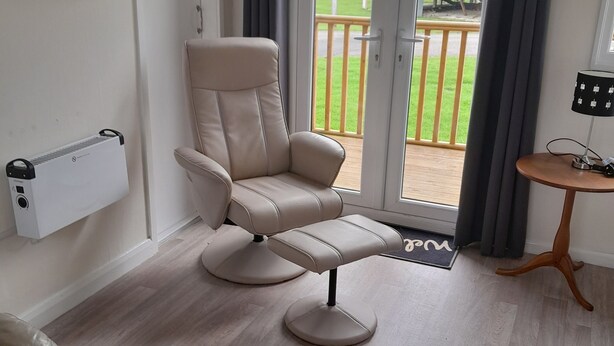 Ett modernt vardagsrum med en beige lädersoffa, en fåtölj, ett litet träbord och en tv som är monterad på väggen.