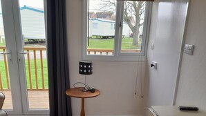 Ett rum med en skjutdörr i glas som leder ut till en balkong, ett litet runt bord med en lampa, en soffa och en liten köksdel med en bänkskiva och en stol.