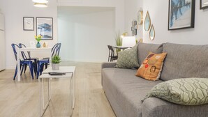 Uma sala de estar moderna com um sofá cinzento, uma mesa de centro e cadeiras azuis. Há uma área de jantar com uma mesa e cadeiras brancas.