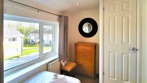A bedroom with a bed, a dresser, a mirror, and a door. - Cornish Getaway (Newquay)