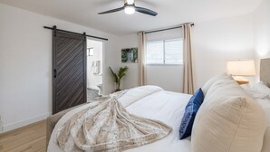 A bedroom with a bed, a ceiling fan, a window with curtains, a bedside lamp, and a door.